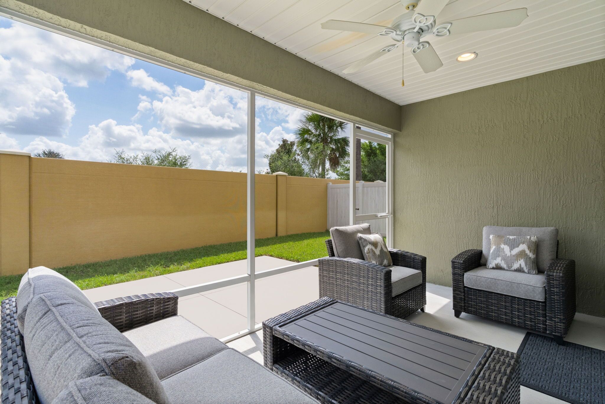 An outdoor patio with wicker furniture, a ceiling fan, and a view of a backyard.