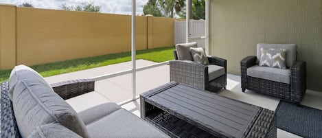 An outdoor patio with wicker furniture, a ceiling fan, and a view of a backyard.