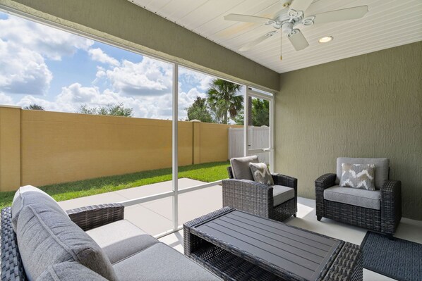 An outdoor patio with wicker furniture, a ceiling fan, and a view of a backyard.