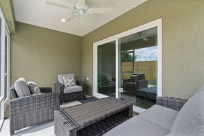 A covered patio area with wicker furniture, a ceiling fan, and a sliding glass door leading to an outdoor space.