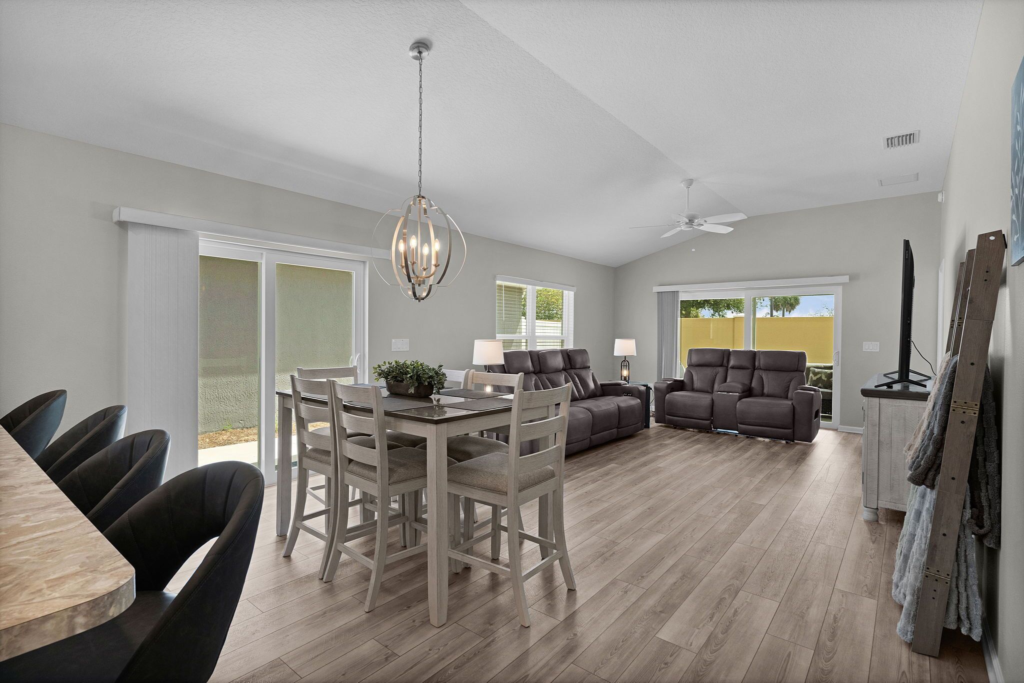A spacious living area with a dining table, chairs, a sofa, and a ceiling fan.