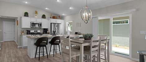 A modern kitchen with white cabinets, stainless steel appliances, and a dining area with wooden chairs and a table.