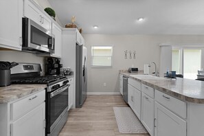 A modern kitchen with stainless steel appliances, white cabinetry, and a wooden floor.