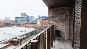 A balcony with a view of a cityscape, a brick wall, and a metal gate. - 1 Bed Apartment, with a balcony city & canal view in Manchester City Centre! By Kammili Properties (Manchester)