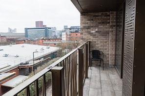 Ein Balkon mit Blick auf eine Stadtlandschaft, eine Ziegelmauer und ein Metallgitter.