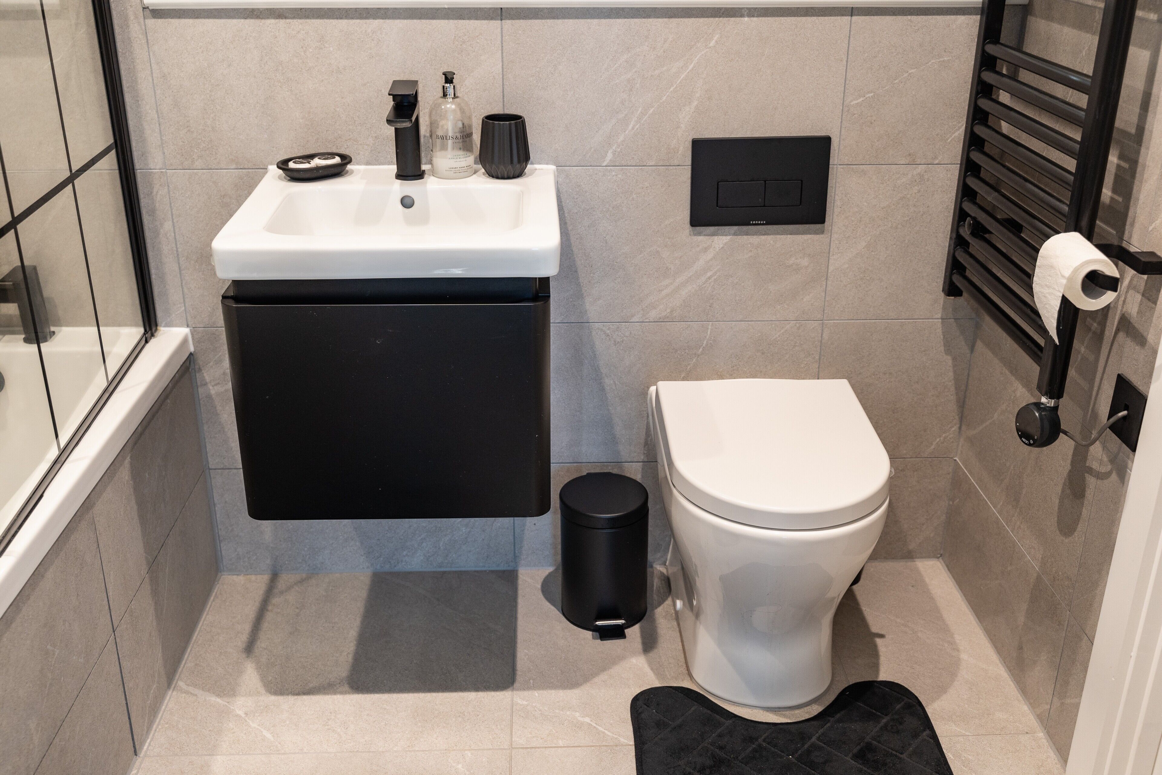 A bathroom with a toilet, a sink, a trash bin, and a towel rack.