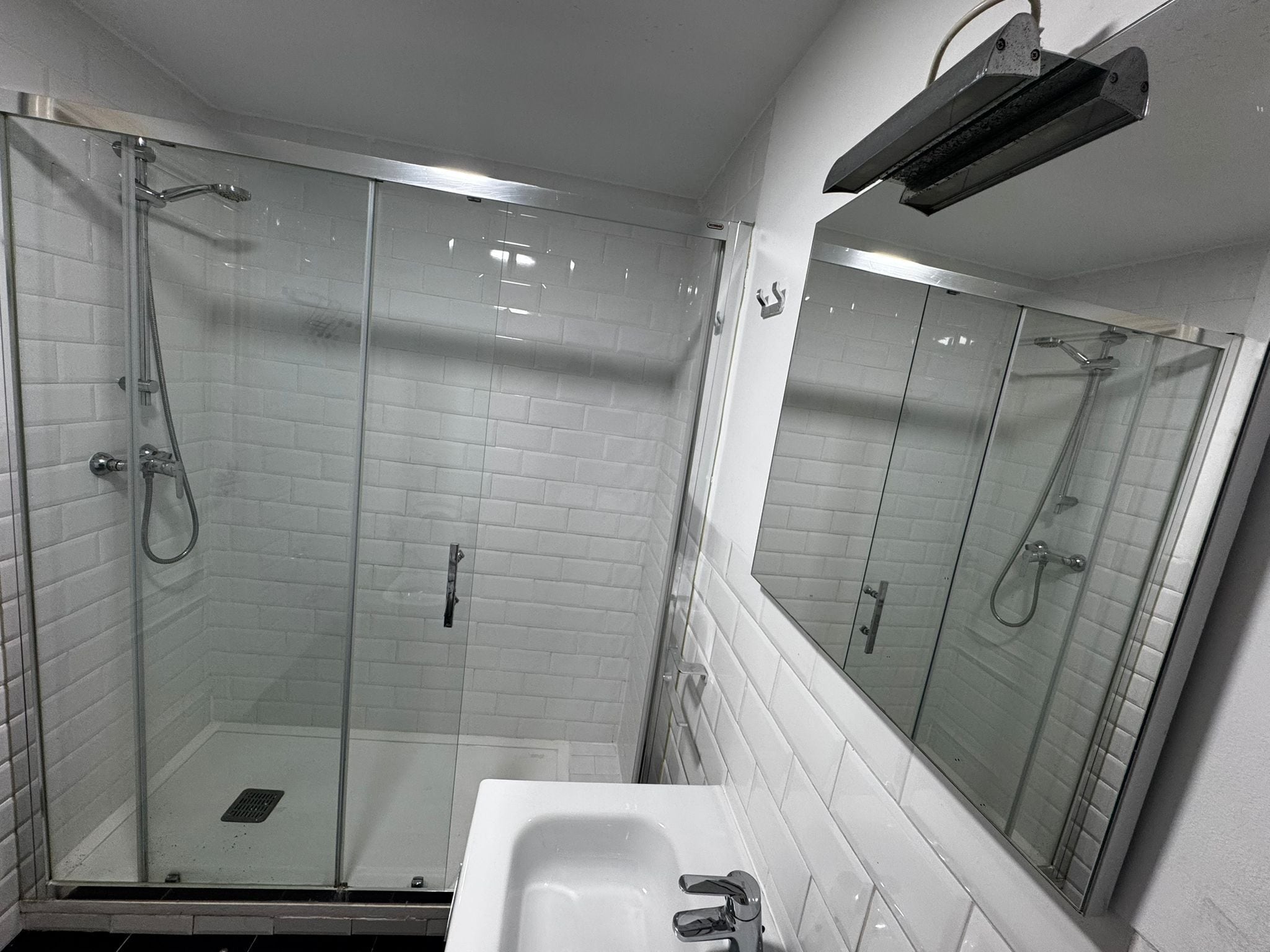Un bany modern amb dutxa de vidre, un lavabo blanc i un mirall.