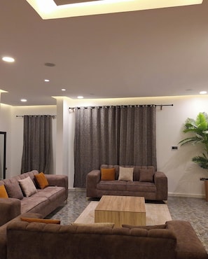 A modern living room with two sofas, a coffee table, and a large window with curtains. - The Royals Apartment  (Ibadan)