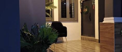 Un intérieur moderne avec un plancher en bois, une chaise noire, une plante en pot et une porte décorée d’une guirlande.