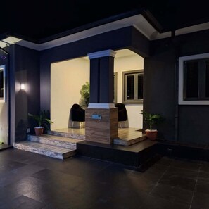 Una zona de recepción moderna con un mostrador de madera, dos sillas negras y plantas en macetas.