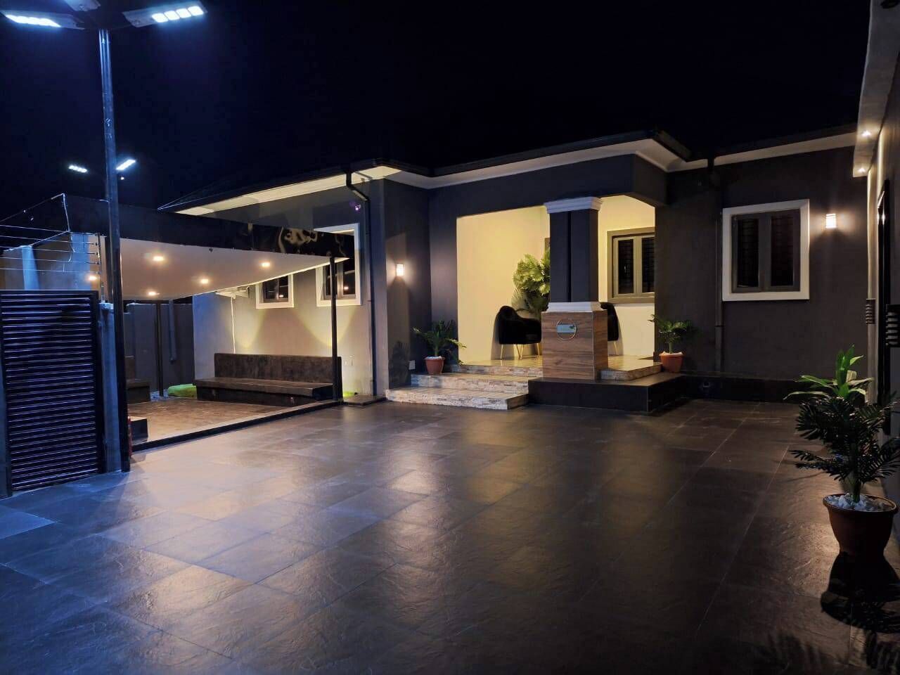 Un espace extérieur moderne, aménagé en patio, avec un coin salon abrité, un petit escalier menant à une porte et des plantes en pot.