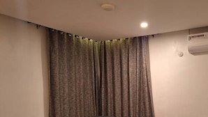 Un dormitorio pequeño y ordenado con cama, una silla y un ventanal con cortinas.