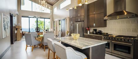 A modern kitchen with a large island, stainless steel appliances, and a high ceiling with exposed beams.
