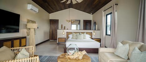 A spacious bedroom with a large bed, wooden ceiling, and a modern chandelier.