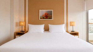 A hotel room with a large bed, two bedside lamps, a framed picture on the wall, and a window providing a view. - w* | Deluxe 1BR w/ Terrace in Barranco (Lima)