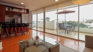 A modern kitchen with a bar area, large sliding glass doors leading to an outdoor patio with a table and chairs. - w* | Deluxe 1BR w/ Terrace in Barranco (Lima)