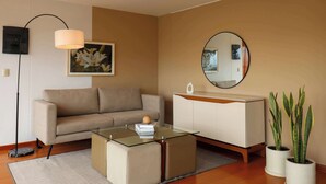 A modern living room with a sofa, a glass coffee table, a white cabinet, a round mirror, a floor lamp, and a potted plant. - w* | Deluxe 1BR w/ Terrace in Barranco (Lima)
