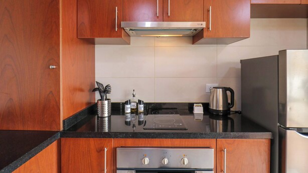 A kitchen with wooden cabinets, a stainless steel range hood, a black countertop, a kettle, and a coffee maker. - w* | Deluxe 1BR w/ Terrace in Barranco (Lima)