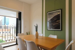 A dining area with a wooden table, white chairs, a vase with a plant, and a framed picture on the wall. - w* | Welcoming 2BR w/ Balcony in Miraflores (Miraflores)