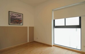 Ein Zimmer mit großem Fenster, einem gerahmten Bild an der Wand und Holzboden.