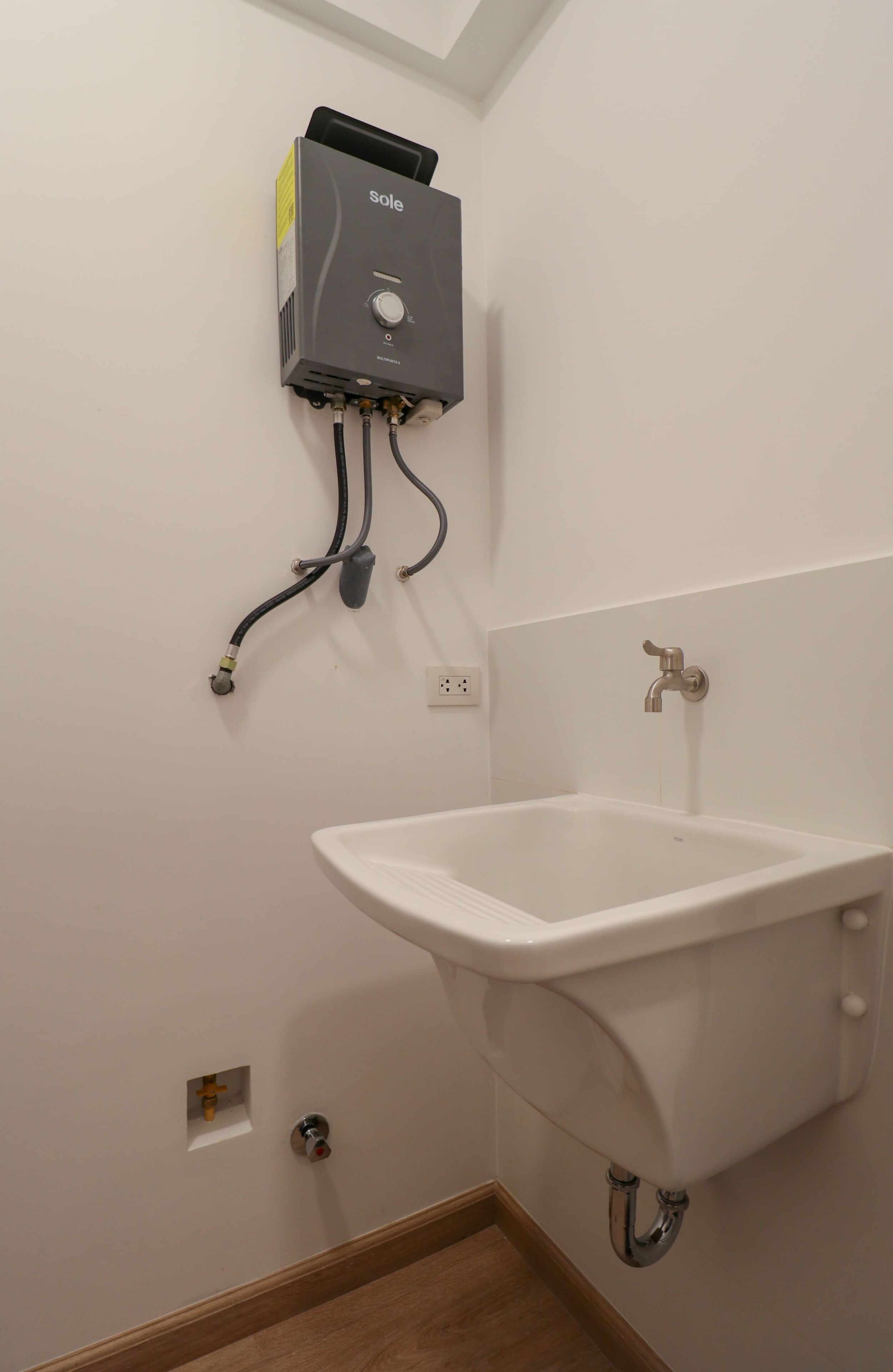 A bathroom with a white sink, a wall-mounted heater, and a visible electrical outlet.