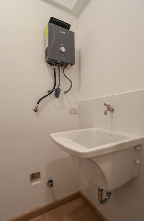 Une salle de bain avec un lavabo blanc, un radiateur fixé au mur et une prise électrique visible.