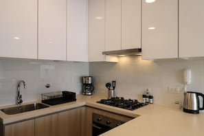 Uma cozinha moderna com armários brancos, uma pia de aço inoxidável, uma cafeteira e uma chaleira.