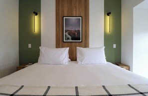 Quarto de hotel com uma cama grande, duas mesas de cabeceira, um criado-mudo, um quadro na parede e duas luzes de parede.