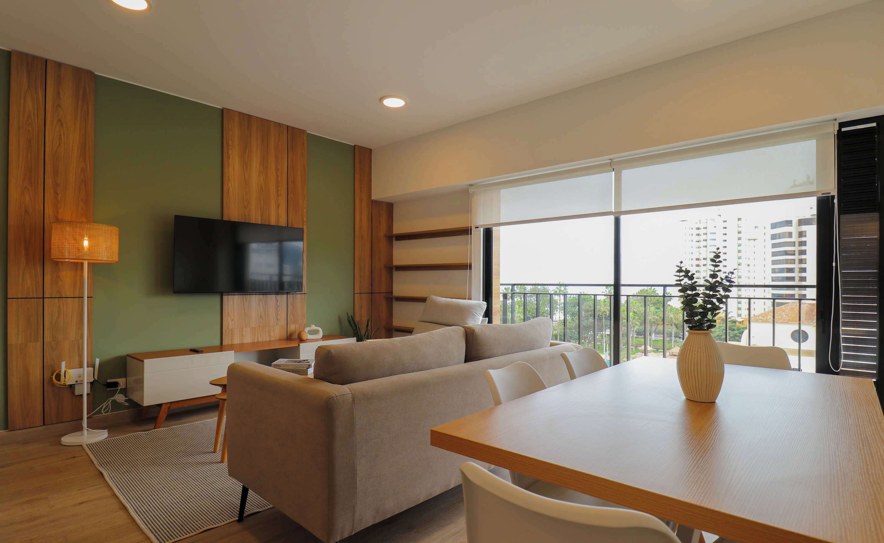 A modern living room with a sofa, a dining table, and a TV mounted on the wall.