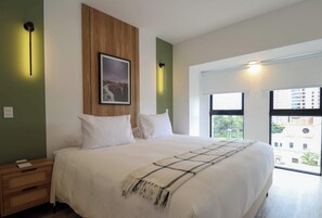 A modern bedroom with a large bed, a wooden panel wall, a framed picture, and a view of buildings through a window. - w* | Welcoming 2BR w/ Balcony in Miraflores (Miraflores)