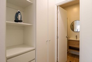 Um armário branco com prateleiras e uma porta que dá para um banheiro com pia e espelho.