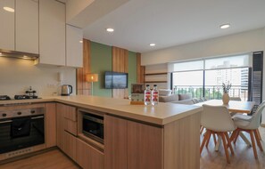 A modern kitchen with a central island, a dining area with a table and chairs, a flat-screen TV mounted on the wall, and a large window offering a view of the city. - w* | Welcoming 2BR w/ Balcony in Miraflores (Miraflores)