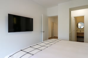 Quarto com cama, televisão montada na parede e porta para o banheiro.