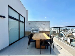 A rooftop terrace with a dining table and chairs, a built-in grill, and a city view. - w* | Upscale 3BR w/ Balcony in Upscale Miraflores (Miraflores)