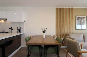 Een moderne keuken met witte kastjes, een eettafel met stoelen, en een zithoek met een bank en een kaart aan de muur.