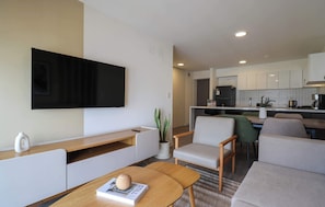 Een moderne woonkamer met een flatscreen televisie, een salontafel met een boek en een decoratief object, en een zithoek met een bank en fauteuils.