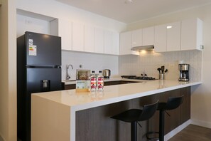 A modern kitchen with a black refrigerator, white cabinets, a large island with bar stools, and a coffee machine. - w* | Upscale 3BR w/ Balcony in Upscale Miraflores (Miraflores)