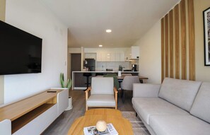A modern living room with a flat-screen TV, a sofa, a coffee table, and a kitchen in the background. - w* | Upscale 3BR w/ Balcony in Upscale Miraflores (Miraflores)