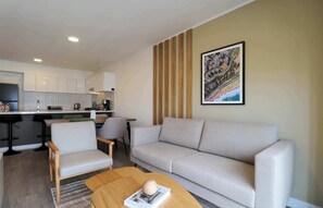 A modern living room with a sofa, armchairs, a coffee table, and a kitchen in the background. - w* | Upscale 3BR w/ Balcony in Upscale Miraflores (Miraflores)