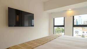 Ein Schlafzimmer mit einem Bett, einem an der Wand montierten Fernseher und einem großen Fenster mit Blick auf Gebäude.