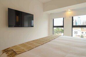 A bedroom with a bed, a television mounted on the wall, and a large window with a view of buildings. - w* |  Airy 2BR w/ Balcony in Prime Miraflores (Miraflores)