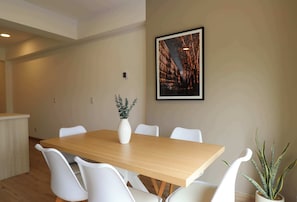 A dining area with a wooden table, white chairs, a vase with green plants, and a framed picture on the wall. - w* |  Airy 2BR w/ Balcony in Prime Miraflores (Miraflores)