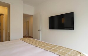 A hotel room with a bed, a television mounted on the wall, and a door leading to another room. - w* |  Airy 2BR w/ Balcony in Prime Miraflores (Miraflores)