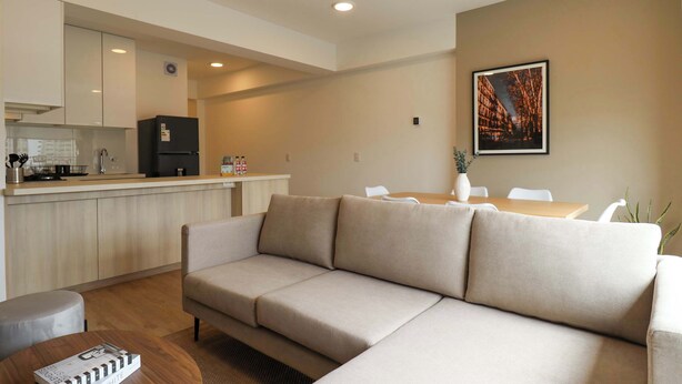 Ein modernes Apartment mit einer Küchenzeile, einem beigefarbenen Sofa, einem Esstisch und einem gerahmten Bild an der Wand.