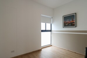 Une pièce avec une grande fenêtre, un tableau au mur et un plancher en bois.