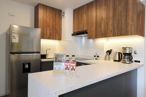 A modern kitchen with wooden cabinets, a stainless steel refrigerator, a coffee maker, and two bottles of a beverage. - w* | Prime 2BR w/ Balcony in Miraflores (Miraflores)