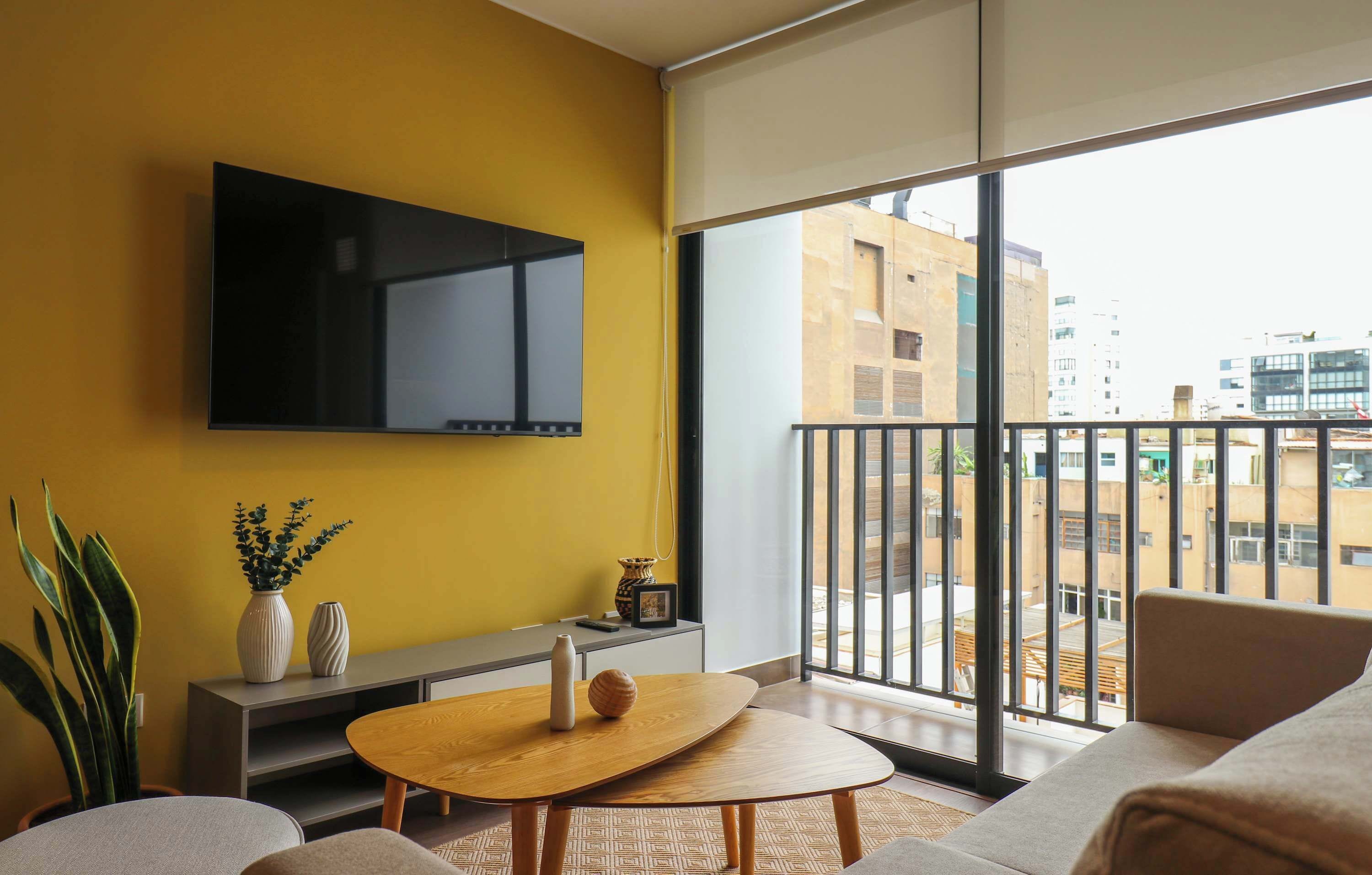 A modern living room with a large TV, a sofa, a coffee table, and a balcony with a city view.