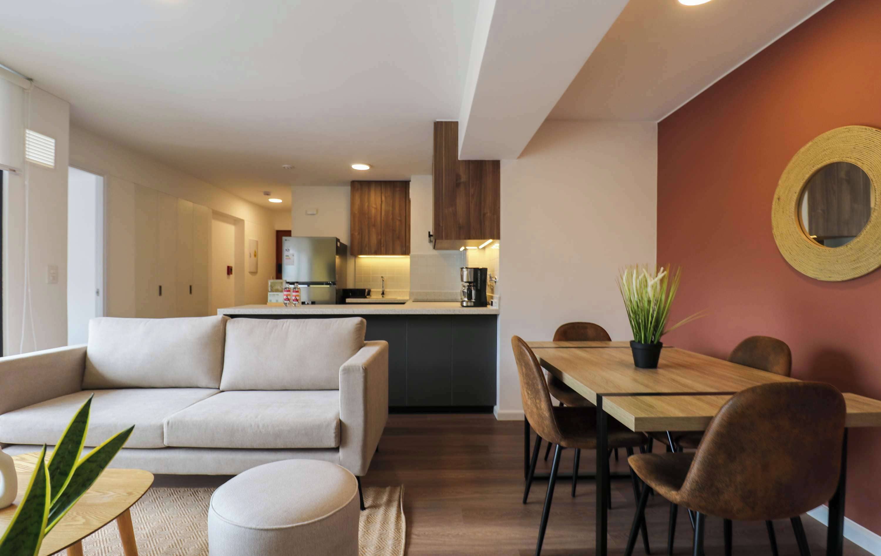 A modern living room with a sofa, a dining table with chairs, and a kitchen area in the background.