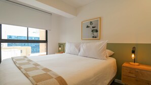 A hotel room with a large bed, a bedside table with a lamp, a window with a view of buildings, and a framed picture on the wall. - w* | Prime 2BR w/ Balcony in Miraflores (Miraflores)