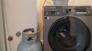 A compact laundry setup with a washing machine and a gas cylinder, connected to a wall-mounted heater. - w* | Prime 2BR w/ Balcony in Miraflores (Miraflores)
